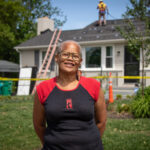 A woman stands in front her her home while solar panels are installed