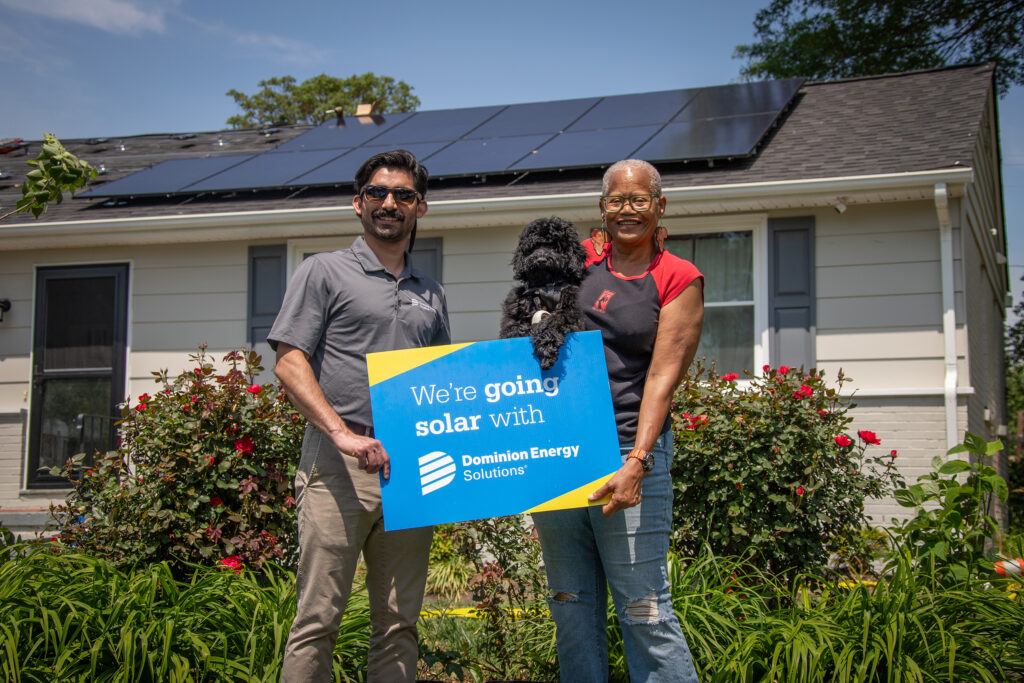 A Dominion representative stands with the solar panel home owner and her dog.