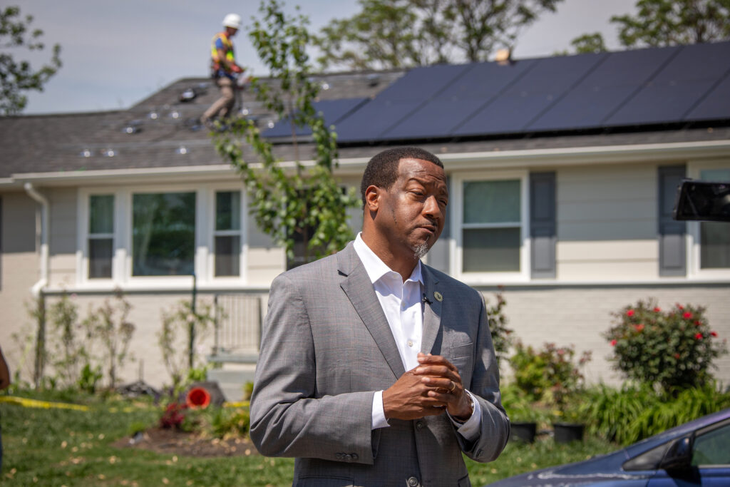 Tyrone Nelson stands in front of a home having solar panels installed.