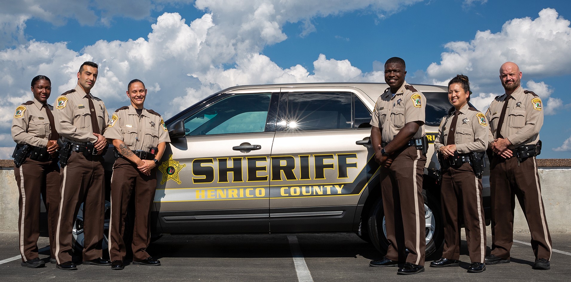 Group of men and women in uniform standing in front of a car.