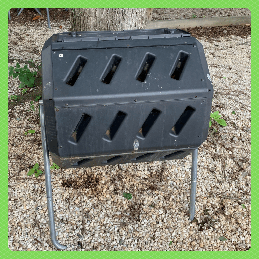 Photo of a black, cylindrical compost bin held off the ground by a metal stand.