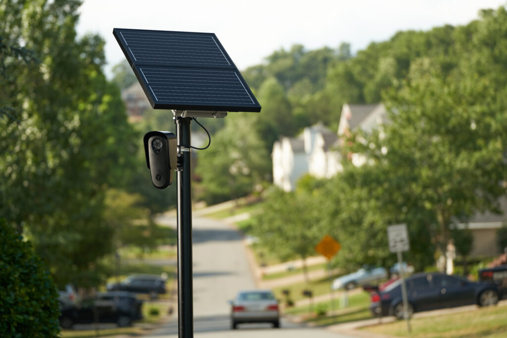 Image shows a Flock Safety Camera attached to a pole with a solar panel on it.