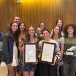 A photo of members of a high school girls cross country team posing with plaques recognizing their state title.
