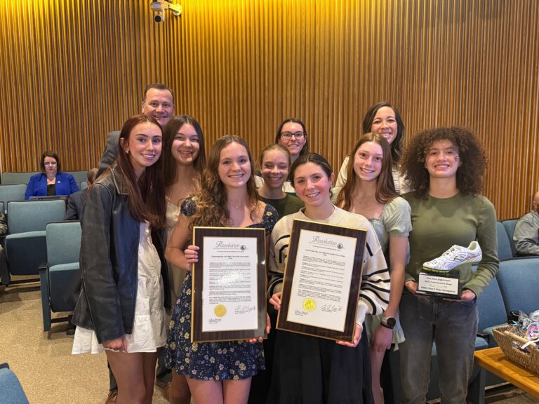 A photo of members of a high school girls cross country team posing with plaques recognizing their state title.