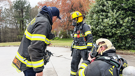 Three firefighters, in full gear, talking outside.