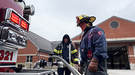 Firefighter wearing full gear standing in front of a fire engine.