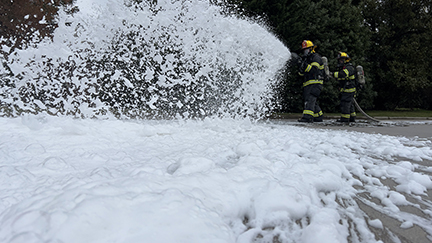 Two firefighters spraying foam far away.