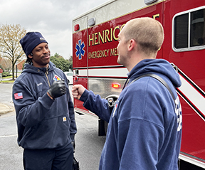 Two firefighters greeting each other near a firetruck.