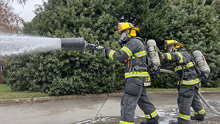 Two firefighters, in full gear, spraying special fire foam, outside, for practice