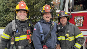 Three firefighters, in full gear, standing and smiling.