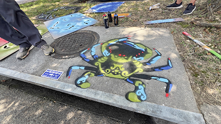 A blue crab painted on the top of a storm drain.