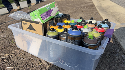 A white plastic container holding  many paint spray cans of multiple colors 