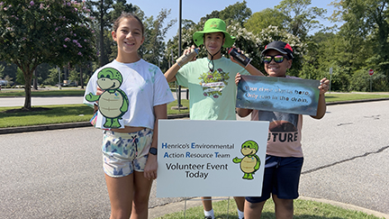 3 teenage girls behind a HEART volunteer sign, holding Stewart the eco-turtle, spray paint cans & a template