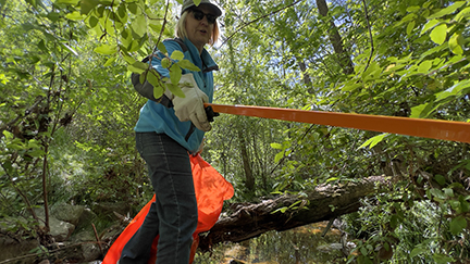 Woman holding a trash bag and picking up trash in the forest