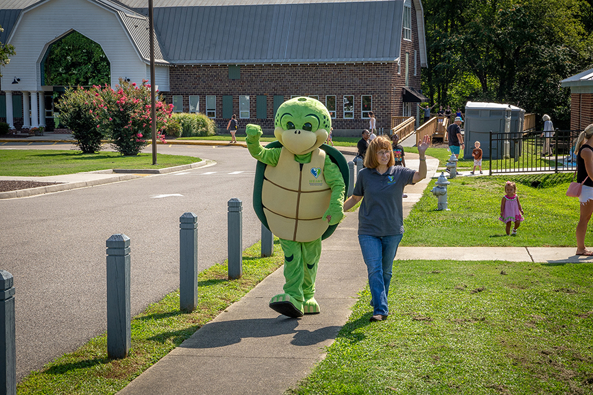 Lifesize Stewart the Turtle mascot walking and holding hands with another H.E.A.R.T employee as they both wave