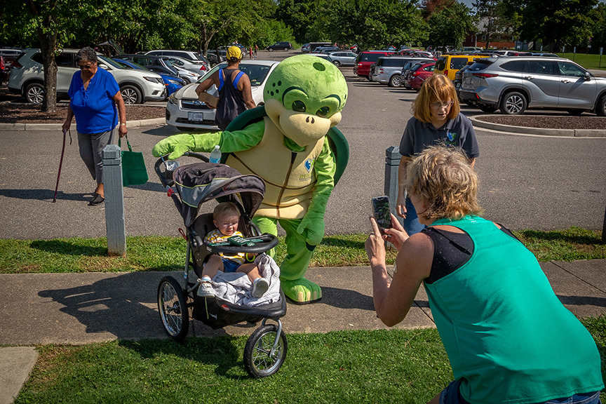 Lifesize Stewart mascot bends next to a baby in a stroller as the mom takes a picture