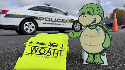 Stewart the turtle mascot cutout standing on pavement with a police car behind him