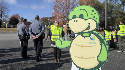 Stewart the turtle mascot cutout in behind a group of police officers & people wear reflective vests