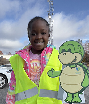 Stewart the turtle mascot cutout with a young girl wearing reflective vests