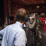 Man behind TV camera looking at a speaker at a podium