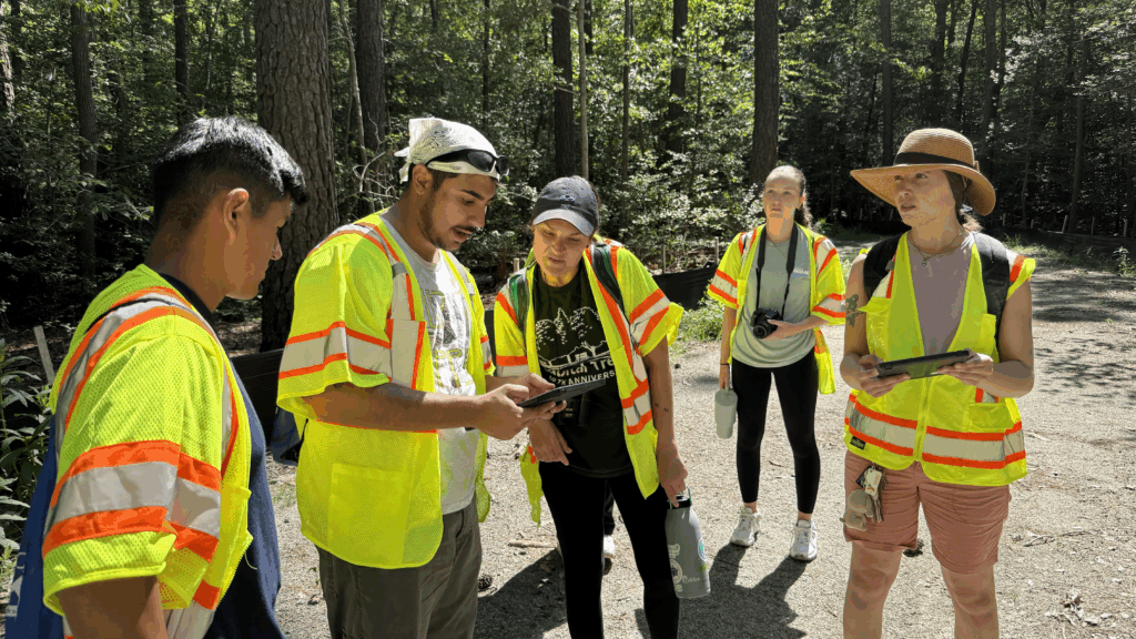 A photo of five people in yellow vests looking at an iPad. 
