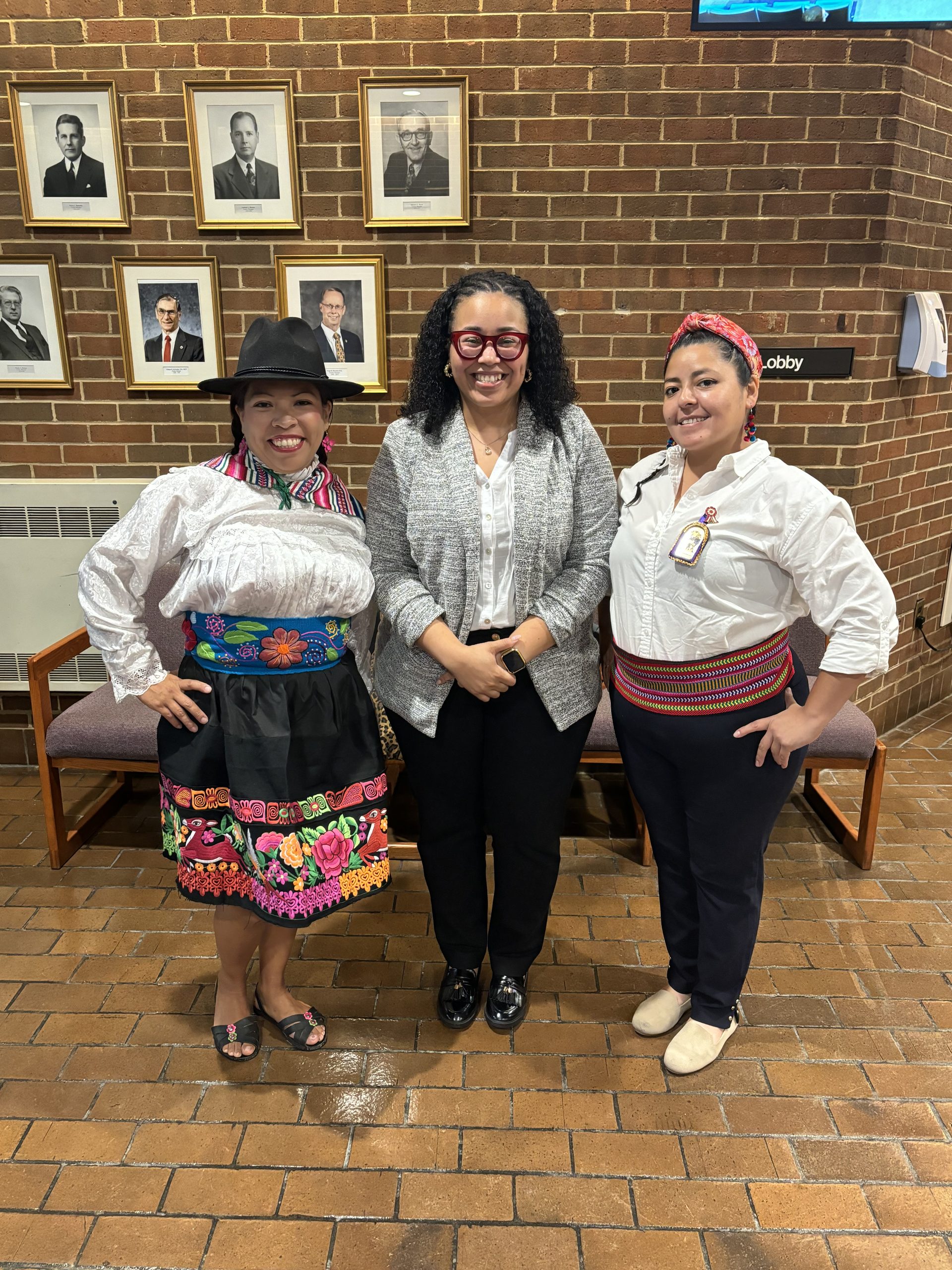 Three women standing side by side. Two women on the outside have on traditional Peruvian clothing. 