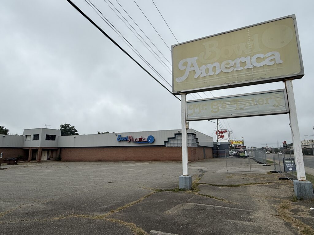 A deserted parking lot with a large, faded sign in front labeled "Bowl America." The building displays the "Bowl America" logo, and the surrounding area appears overcast.