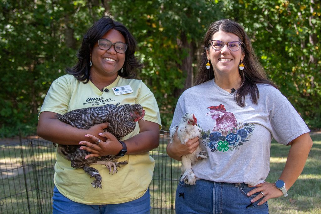 Two people stand pose for a photo while holding adult hens.