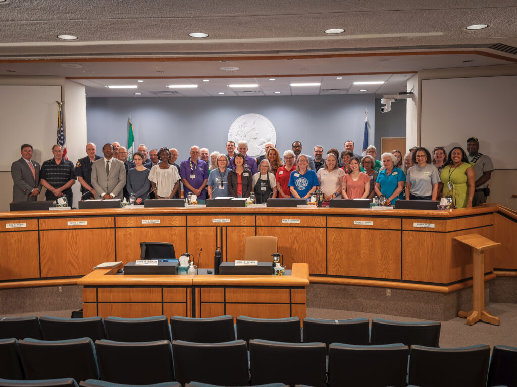 Volunteers stand with officials behind the meeting room dais to celebration Volunteer Week.
