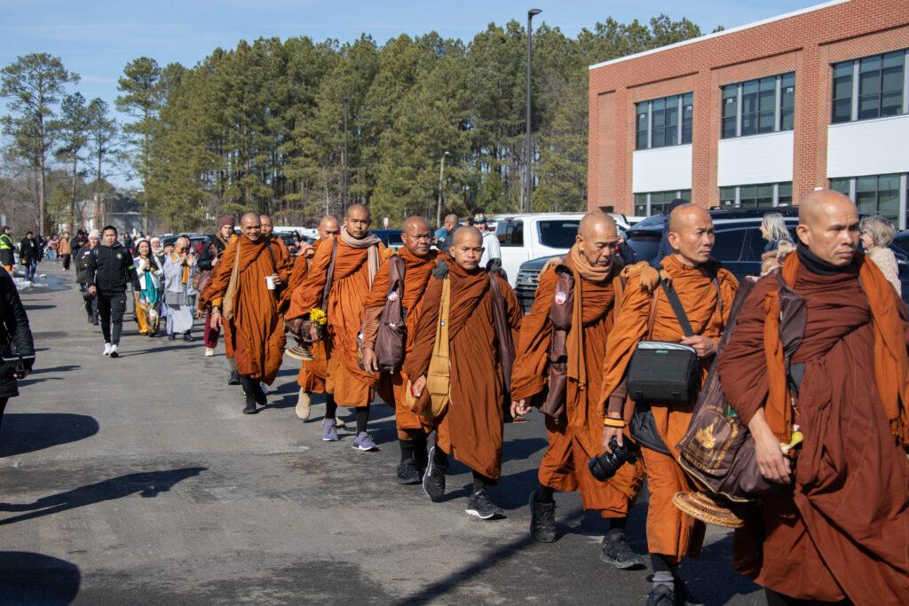 Many monks walk in a line to a building.