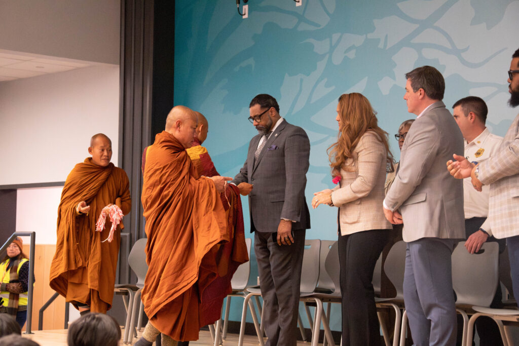 A photo of a monk exchanging greetings with county officials on a stage.