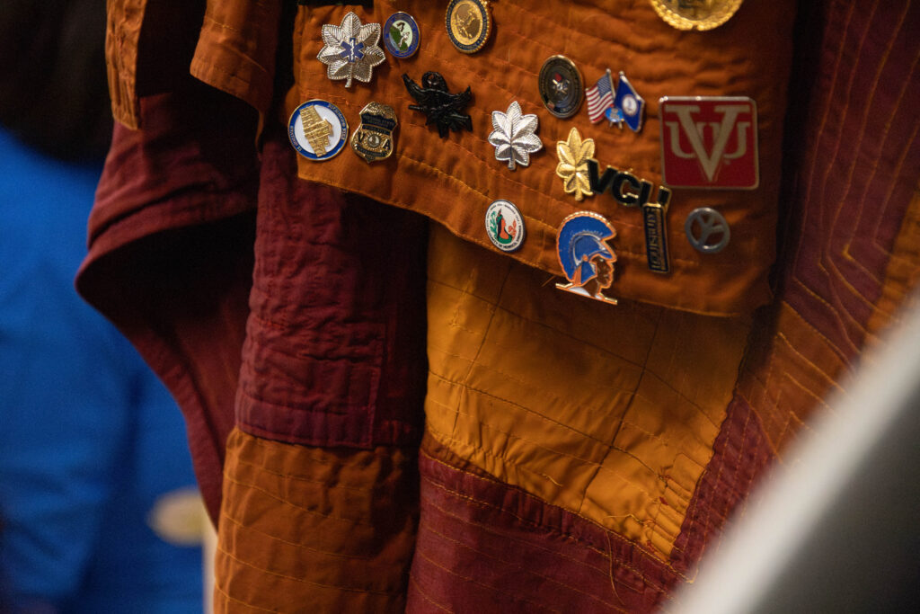 The orange and red robes of a monk shows many pins from different localities, including Henrico County.