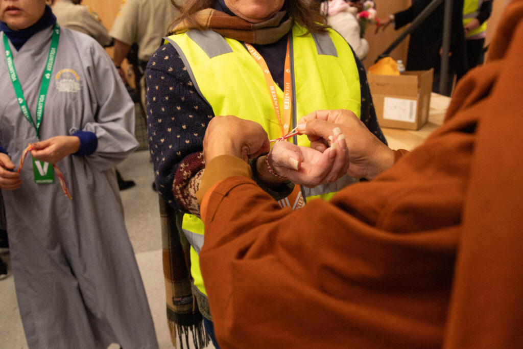 A woman holds her arm out for someone to tie a braided bracelet onto her wrist.