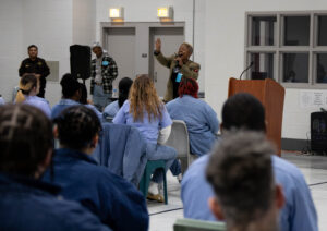A woman speaks to a crowd of inmates in a jail.