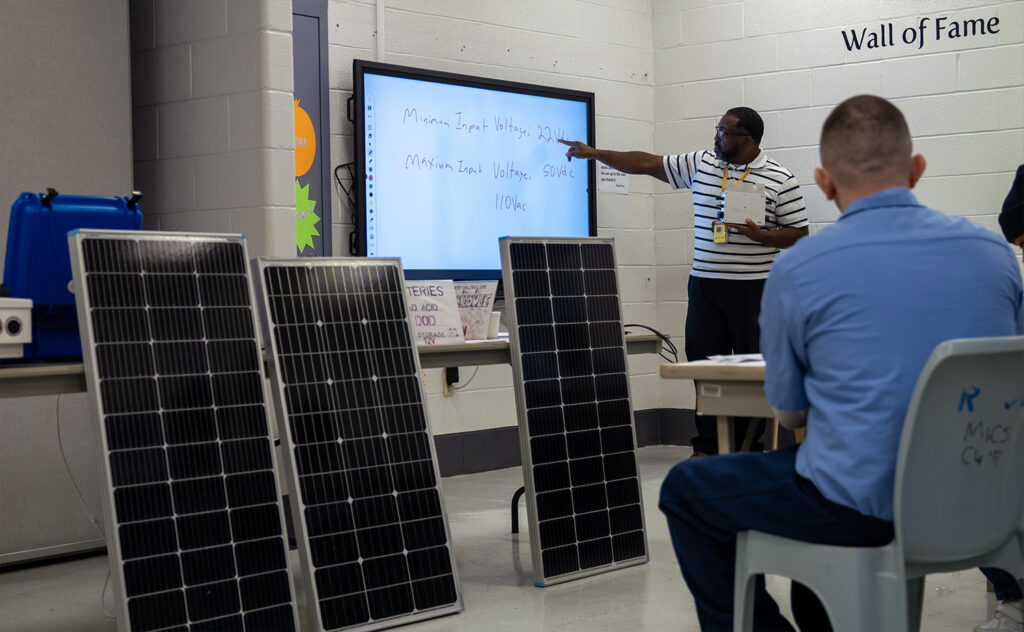 A photo of a man pointing at a screen behind solar panels. 