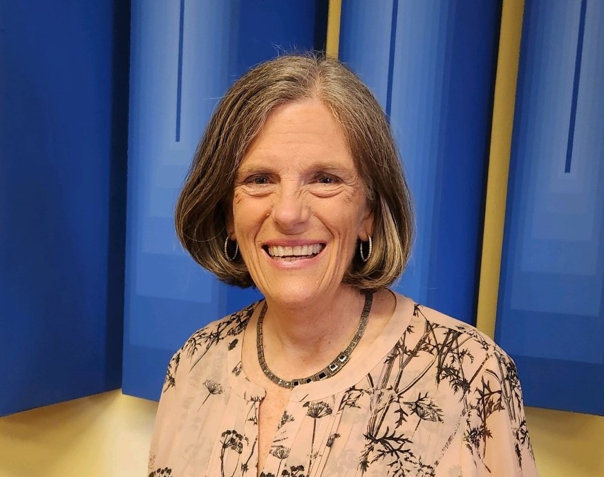 A woman with shoulder-length hair standing in front of blue backdrop.
