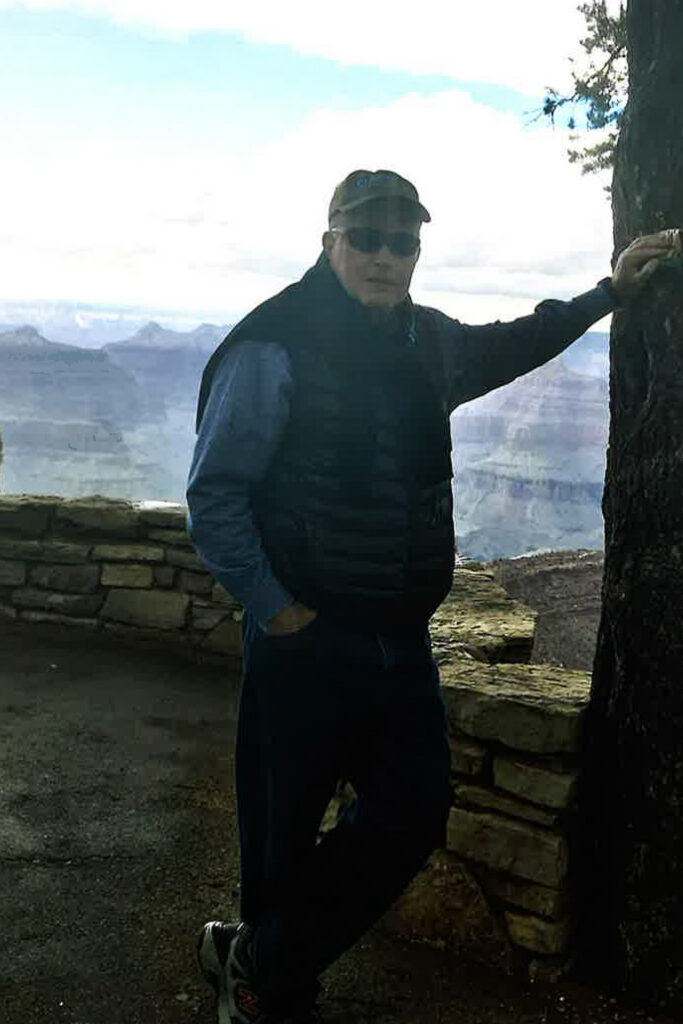 A man poses next to a tree on a mountain hike.