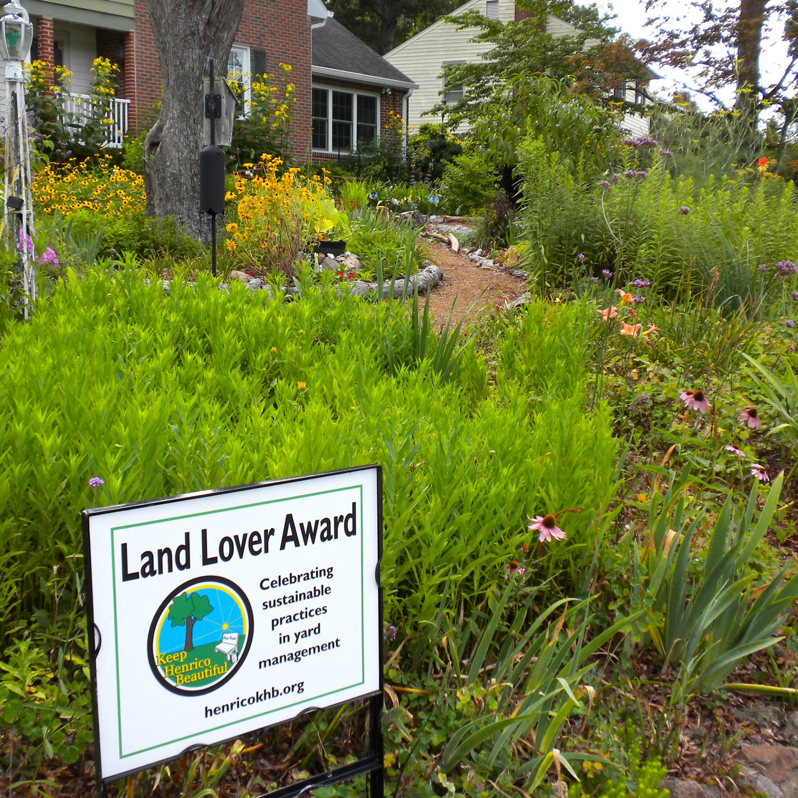 A lush yard filled with tall, green, native grasses and flowers. A white sign says "Land Lover Award" and contains the Keep Henrico Beautiful Logo.