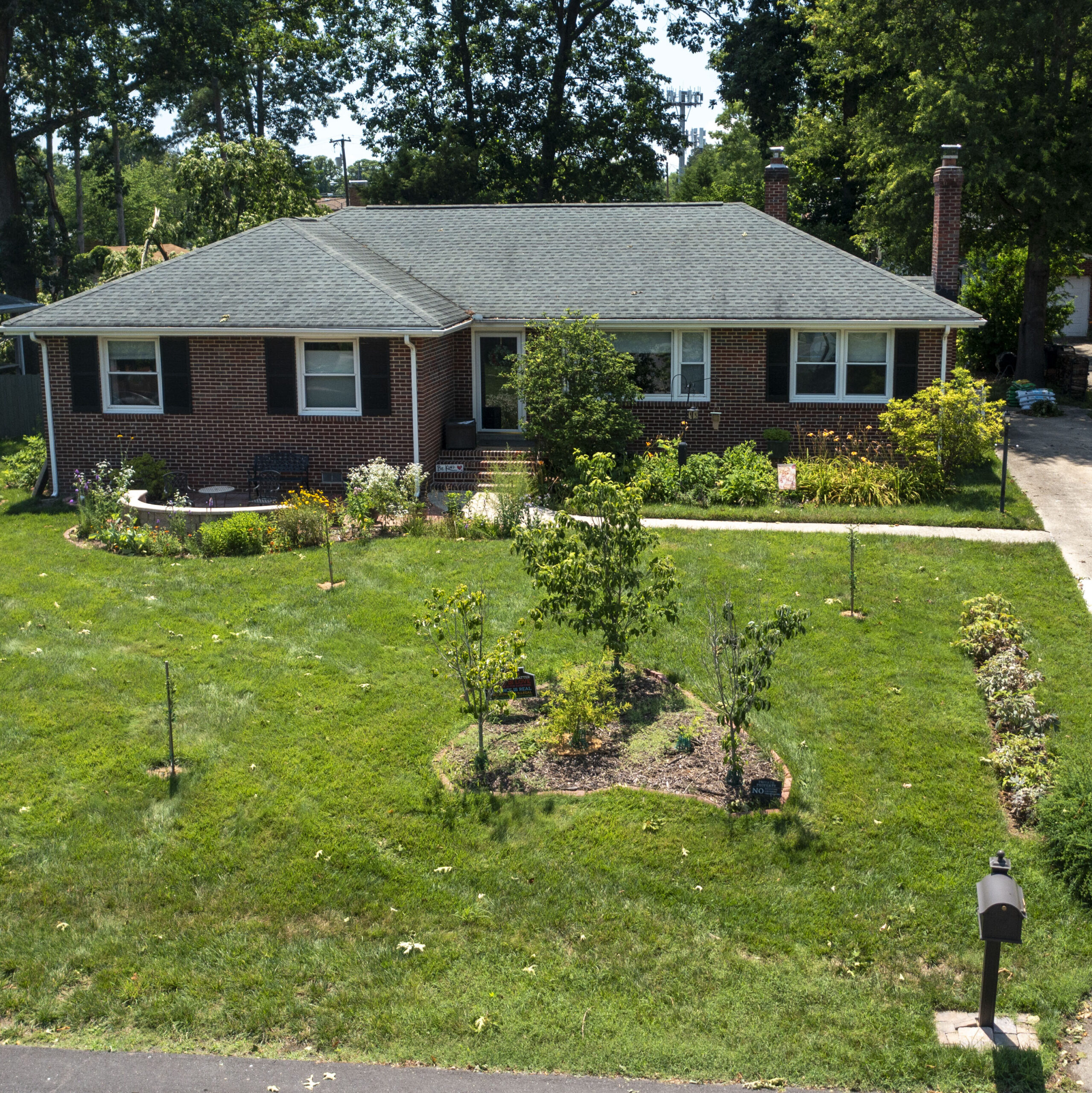 aerial photo of a brick house with a well kemp front yard containing many shrubs and young trees.
