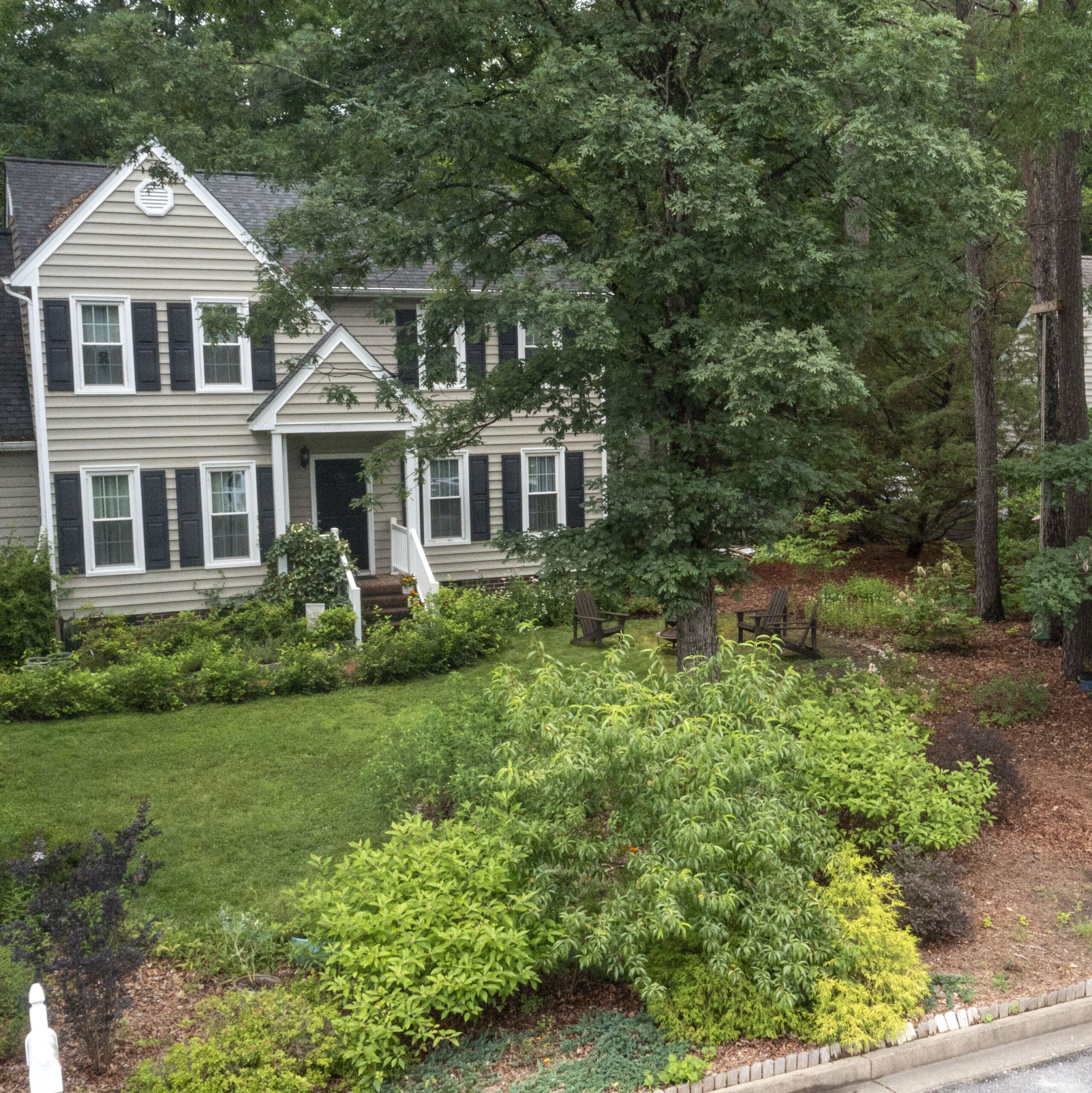 photo of a house with a well kemp front yard filled with large, mulched garden bed full of native shrubs and flowers.