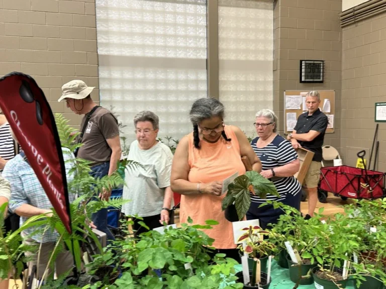 Event attendees browse various plants on a table, inspecting the label descriptions.