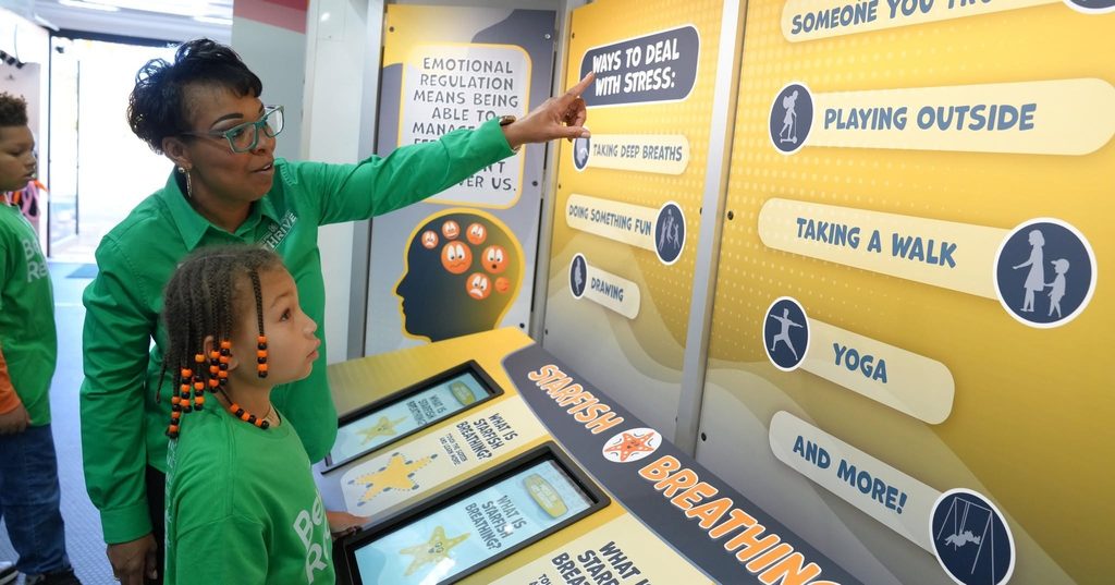 Woman points to show young female student educational display on Virginia 4-H Mobile Learning Lab.