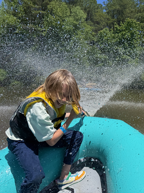 A boy in a raft getting sprayed by a water fountain.