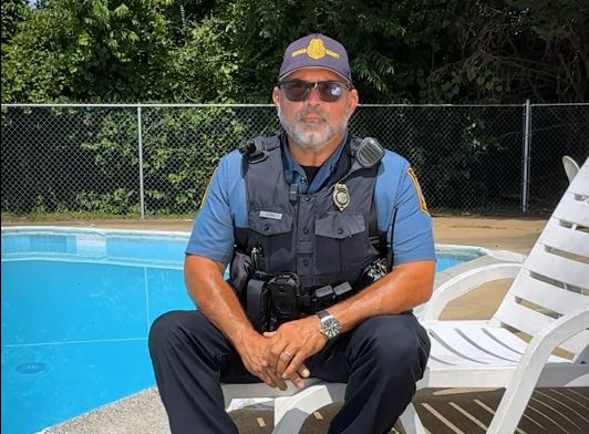 Henrico Police Officer in uniform sits on a pool chair next to a pool.