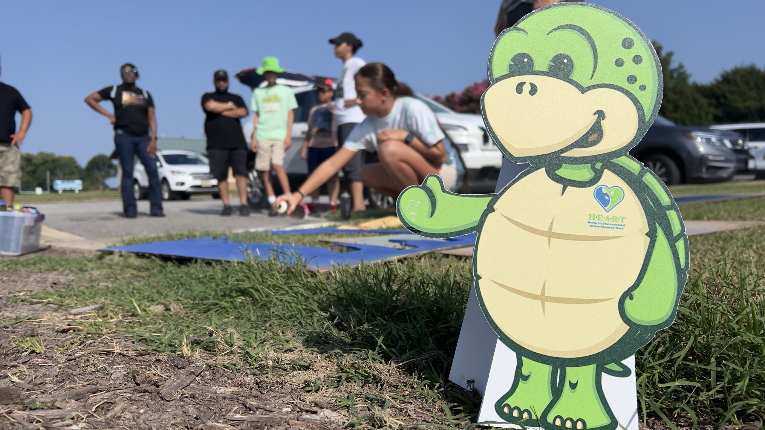 Stewart the turtle, HEART mascot, in front of people painting storm drains