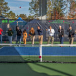 Photo of 12 people involved with building and procuring the pickleball courts hitting a pickleball