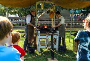 Photo of two men demonstrating blacksmithing at the Red, White, and Lights Event. 
