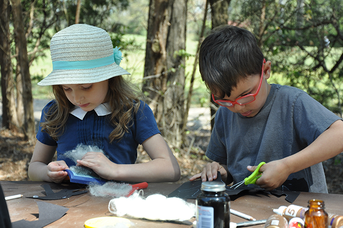 A girl and boy sitting outside cutting paper and pulling wool.