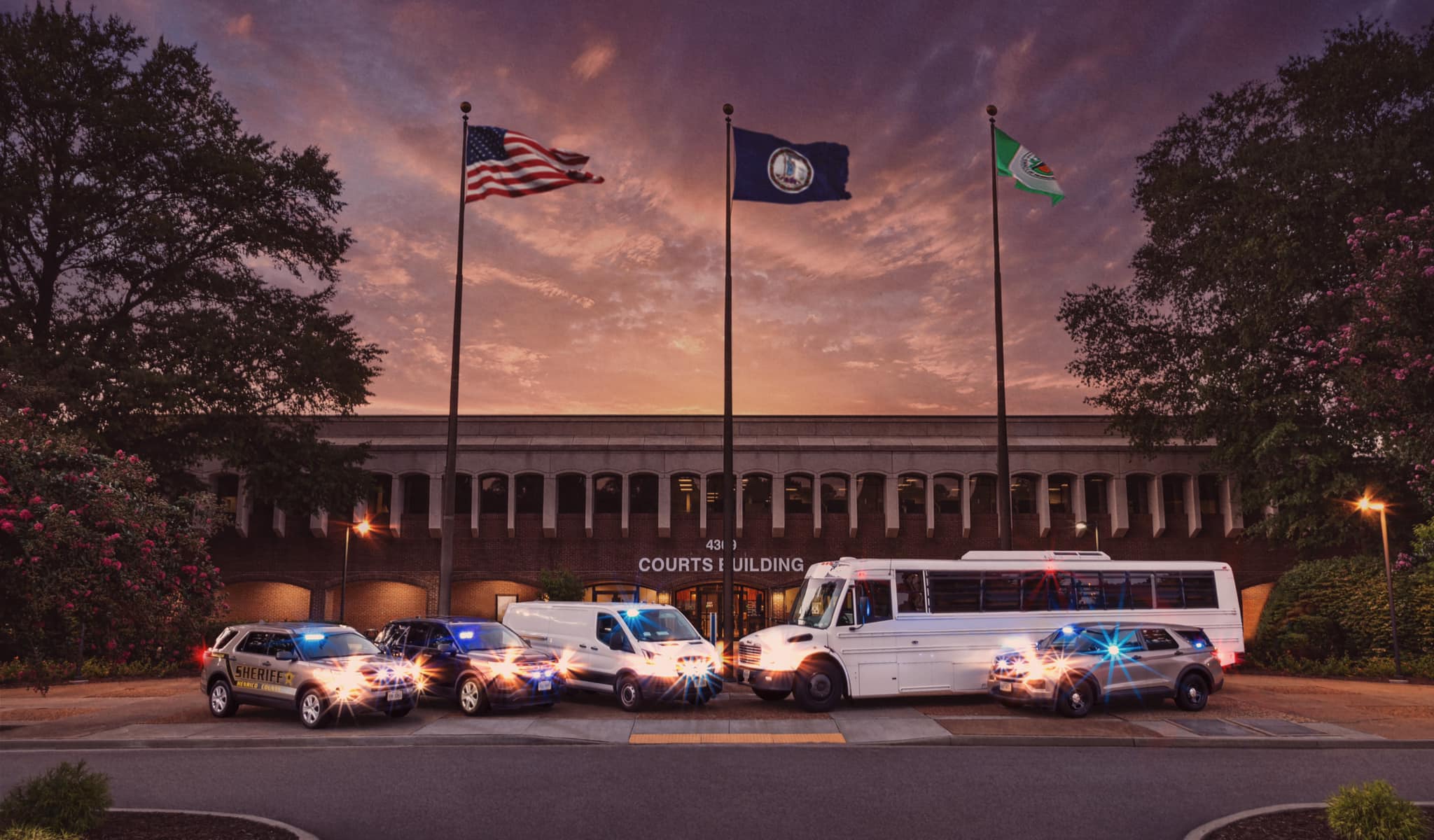 Image shows several vehicles belonging to the Sheriff's Office in front of the Henrico County courts building with a beautiful sunset.