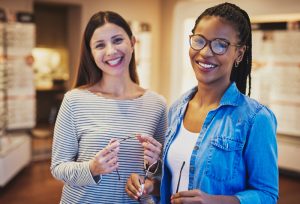 two women smiling as they try on eye glasses